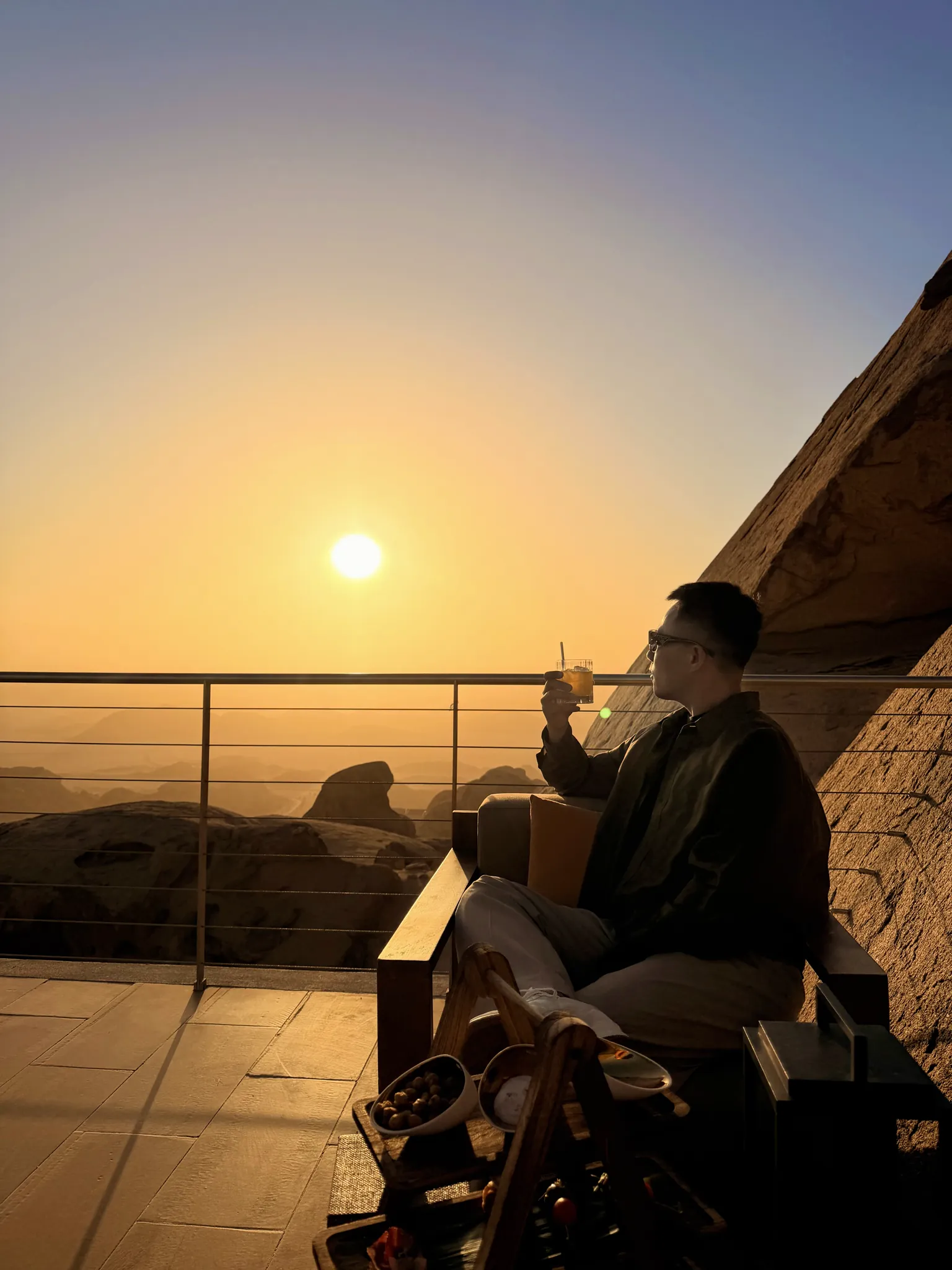 男子在悬崖露台凭栏远眺夕阳的剪影